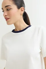 Remera blanca de algodón con cuello redondo y mangas cortas. El cuello es de color azul marino en contraste.