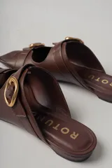 Sandalias planas de cuero color marrón con dos tiras anchas sobre el empeine, cada una con hebilla dorada.