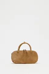 Bolso mini marrón de serraje con estilo bowling, doble asa corta y correa bandolera extraíble. Tiene pespuntes en el cuerpo, bolsillo interior con cremallera y cierre con cremallera.