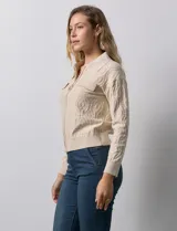 Cardigan color beige en tejido jacquard, con cuello con solapa y abertura central con cierre. Delantera con bolsillos simulados.