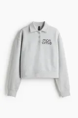 Remera polo gris de corte holgado en tejido felpa liviana con cuello y tapeta de botones. Modelo de manga larga con hombros caídos y ribete acanalado en puños y bajo.