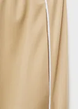 Pantalón de vestir color beige, de corte recto y tiro medio, con cintura elástica y bolsillos laterales. Presenta una raya vertical blanca a lo largo de la pierna.