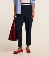 Pantalón de vestir azul marino, de corte zanahoria, con cinturón fino negro con hebilla dorada.