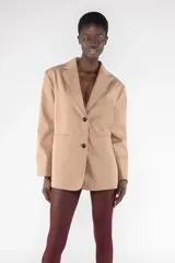 Blazer color beige de corte holgado, con solapas y bolsillos de ribete. Tiene un bolsillo de parche en la parte posterior y un parche con el logotipo de gabardina.