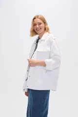 Chaqueta blanca de algodón con cuello camisero, cierre frontal con botones, bolsillos de parche y frunces en los hombros.