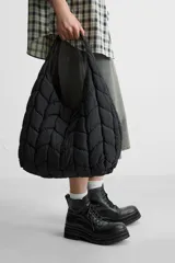 Bolso de hombro negro fabricado en tejido técnico acolchado con diseño geométrico. Tiene un compartimento principal con cierre mediante imán, un bolsillo plano y un bolsillo con cierre mediante cremallera en el interior.