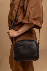 Bandolera negra de cuero sintético con correa larga regulable y bolsillo frontal con cierre.