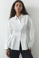 Camisa blanca de cuello solapa y manga larga. Detalle de pliegues con botones. Cierre frontal con botones.
