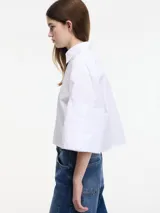Camisa blanca cropped con botones en la parte delantera y mangas 3/4 con botones. Tiene pinza en la espalda.