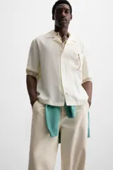 Camisa negra de corte relaxed fit, confeccionada en tejido con mezcla de modal. Tiene cuello bowling, manga corta, bolsillo de parche en el pecho y cierre frontal con botones.