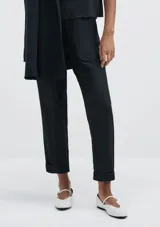 Pantalón negro de tiro alto con cintura elástica fruncida y bolsillos tipo parche redondeados en la parte delantera. El corte es recto y el bajo está doblado.