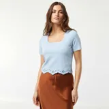 Camiseta celeste de punto con cuello cuadrado y mangas cortas. Presenta un detalle de bordado calado en el bajo.