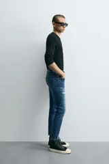 Pantalón de jean azul oscuro con efecto lavado y roturas en las rodillas, de corte ajustado al cuerpo desde la cintura hasta el tobillo.