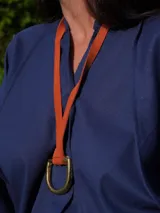 Collar con tira de cuero color suela y dije metálico dorado en forma de estribo.