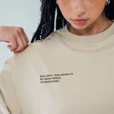 Remera color beige con cuello redondo y estampado con texto en el pecho y logo en la parte inferior.