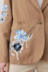 Blazer color tostado con bordados florales en azul y negro en la solapa y en la manga.