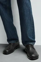 Zapato de vestir de cuero negro, tipo derby con cordones, de horma redonda y suela con ligero tacón.