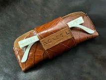 Estuche para lentes color borgoña con textura símil cocodrilo y cierre con broche a presión.