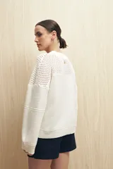 Sweater de punto color salmón con cuello redondo y mangas anchas. Presenta un diseño calado en la parte superior y tejido tramado horizontal en el resto del cuerpo.