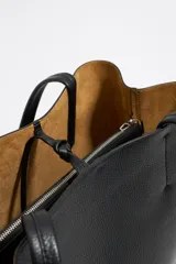 Bolso shopper negro de cuero con textura granulada, doble asa de hombro y logo blanco estampado en la parte inferior. Interior color caramelo con bolsillo con cierre. Cierre superior con lazo de cuero.