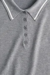 Remera polo corta de punto fino color gris con cuello, tapeta de botones y mangas cortas con ribete blanco.