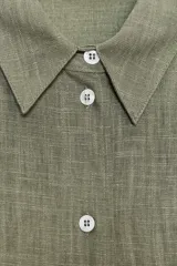 Camisa amplia color negro confeccionada con hilatura de lino. Tiene cuello solapa, manga larga, bolsillo de plastrón en el delantero, bajo asimétrico y cierre frontal con botones.