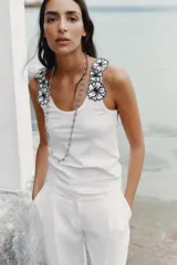Top blanco de algodón con escote redondo y tirantes decorados con apliques de flores negras.