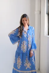 Vestido largo celeste con estampado floral en beige, corte evasé, cuello camisero, mangas largas con volados y falda escalonada.