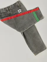 Pantalón de jean celeste con efecto lavado, corte recto y largo a la rodilla. Presenta una cinta vertical color violeta en la pierna izquierda, una cinta vertical color verde en la pierna derecha y una cinta horizontal color rosa en la parte inferior de ambas piernas.