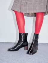 Botas de cuero charol negro con caña media y punta cuadrada. Cuentan con cierre trasero, tirador y bordado contrastante en el empeine. El taco es de madera y la suela de goma.