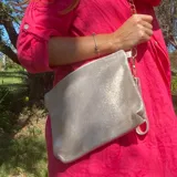 Sobre de cuero vacuno metalizado, con forro interior y bolsillo interno. Incluye correa de cadena desmontable y agarradera de cuero.