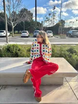 Cárdigan de punto color crudo con botones y ribete rojo. Presenta un patrón de cuadrados de colores (azul, rojo, amarillo y verde).