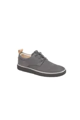 Zapato de vestir estilo derby, color gris oscuro (magnet), confeccionado en gamuza o nobuck. Presenta cordones finos y una suela de goma gruesa y texturizada de color negro con una fina línea blanca que la separa del cuerpo del zapato. Posee un tirador de cuero color camel en el talón.