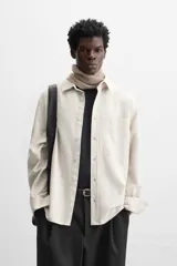 Camisa color crema de corte relaxed fit, confeccionada en tejido de mezcla de algodón suave al tacto. Tiene cuello solapa, manga larga con puños abotonados, un bolsillo de parche en el pecho y cierre frontal con botones.