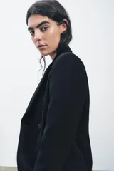 Blazer negro con cuello solapa de muescas y manga larga. Tiene falsos bolsillos de vivo en el delantero, forro interior a tono y cierre frontal cruzado con botón a presión.