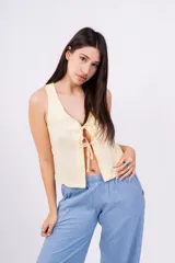 Chaleco corto sin mangas color verde salvia, confeccionado en tela perforada (broderie o calado). Presenta escote en V con lazos ajustables en el centro frontal.