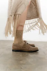 Mocasín de cuero color marrón con tachas metálicas plateadas en la puntera y laterales.
