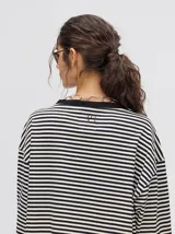 Remera manga larga a rayas horizontales grises y blancas, con cuello redondo rojo y logo bordado en el pecho. Corte holgado.