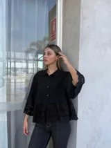 Camisa negra con cuello clásico, cierre frontal con botones, mangas 3/4 con detalle de calado y ruedo con volados y calado.