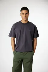 Remera de manga corta color gris oscuro con cuello redondo y un pequeño parche bordado blanco en el pecho.