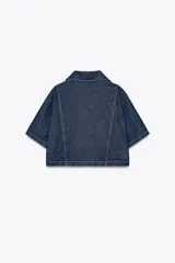 Camisa corta de denim azul con cuello solapa, escote pico, manga corta, bolsillos delanteros de plastrón y cierre frontal con botones metálicos.