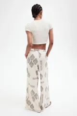 Pantalón de corte holgado en tejido liviano de mezcla de lino y viscosa, color crudo con estampado paisley en marrón. Modelo con cintura elástica fruncida y cordón para ajustar, bolsillos laterales discretos y piernas rectas con bajo deshilachado.