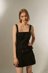 Vestido corto negro con breteles anchos, escote cuadrado, falda con tablas y cinturón con hebilla y ojales.