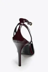 Zapato de tacón destalonado color borgoña, con efecto charol, punta fina y pulsera al tobillo con cierre de hebilla.