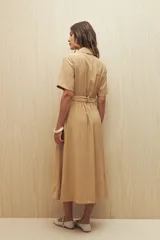 Vestido camisero largo color crema, con cuello camisero, mangas cortas y cierre frontal con botones. Incluye cinturón de la misma tela con hebilla veteada.