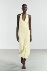 Vestido largo color amarillo pálido, con cuello halter que se ata en la nuca, escote en pico y frunces laterales.