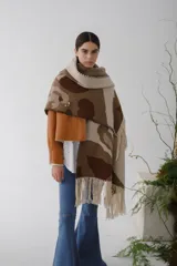 Ruana de lana con diseño abstracto en tonos beige, marrón y blanco. Presenta flecos en el borde inferior y capucha.