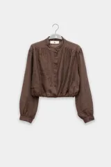 Blusa corta color marrón chocolate en tejido arrugado liviano, con cuello mao, botones al frente y mangas abullonadas. Terminada con ruedo elastizado.