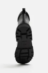 Bota negra de cuero con cordones, suela track y tirador trasero.