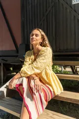 Camisa amarilla con bordado inglés, escote en V, mangas largas abullonadas con puños elásticos y lazos decorativos en el frente.